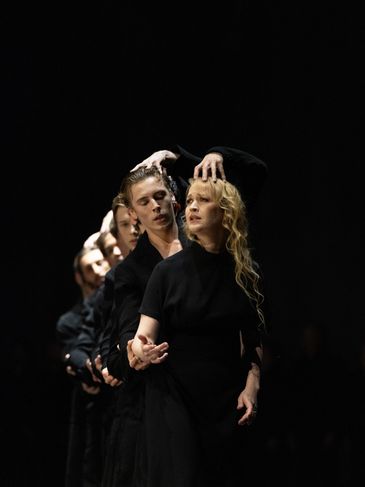 A line of dancers in black performing an expressive routine on stage.