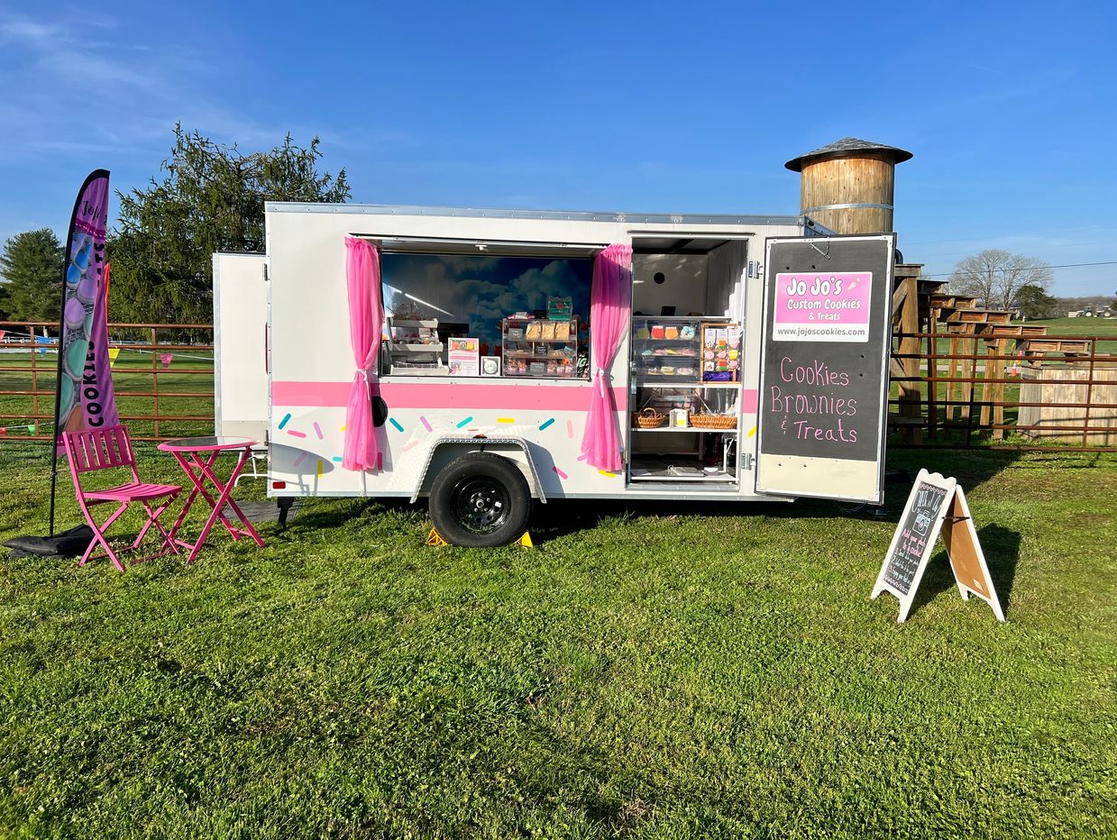 A colorful cookie trailer with pink accents and outdoor seating on a sunny day.