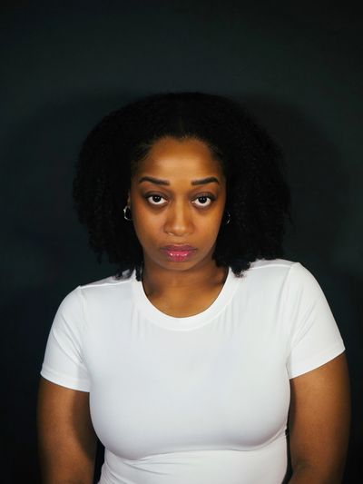Portrait of a woman with natural hair wearing a white shirt against a black background.