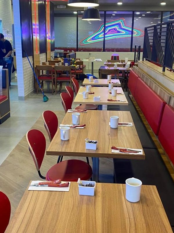 Empty restaurant tables with red chairs and white mugs.