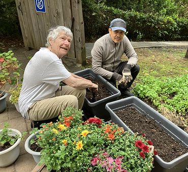 Two men gardening with soil and flowers in containers outdoors.