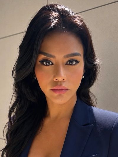 Confident woman with dark hair and bold makeup in a navy blazer.