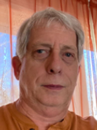 Close-up of a middle-aged man with gray hair wearing an orange shirt.