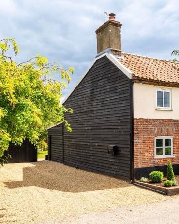 Charming countryside cottage with mixed brick and wood exterior under a cloudy sky.