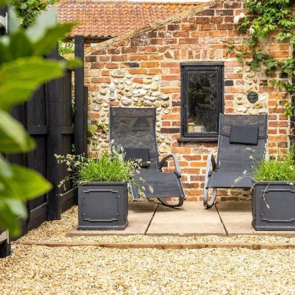 Two black garden chairs with cushions between matching planters in front of a brick wall.