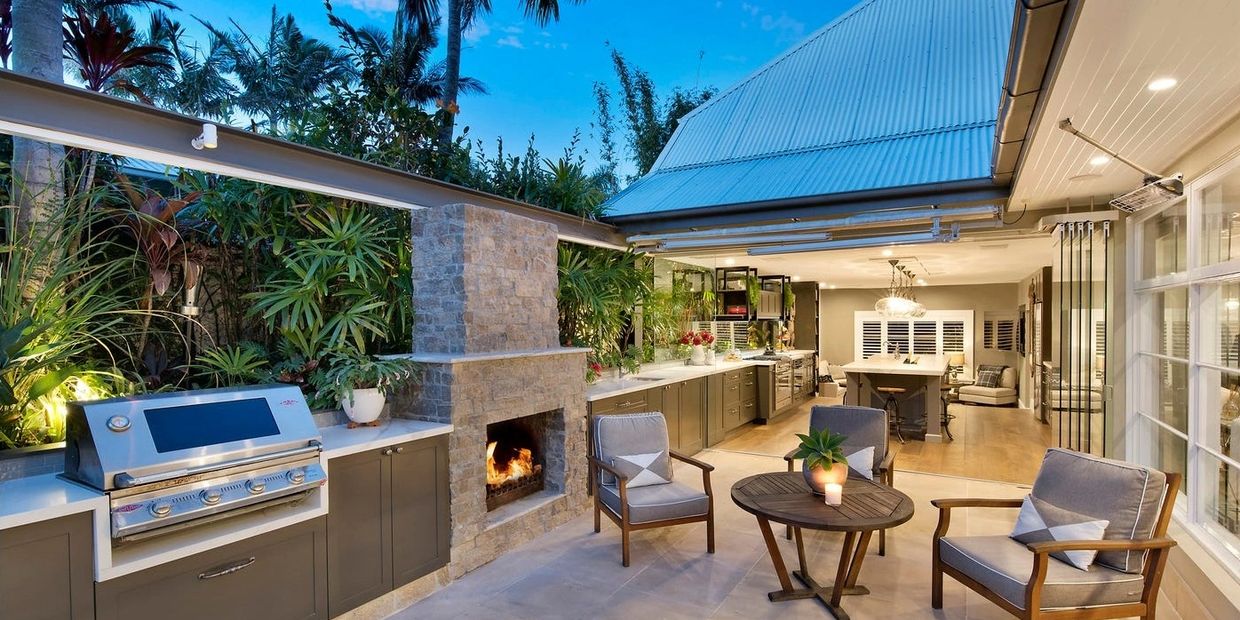 Cozy outdoor kitchen and seating area with fireplace and grill.