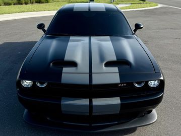 Black Dodge Challenger with grey racing stripes and aggressive front design.