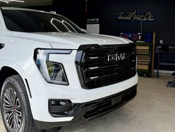 Close-up of a white GMC truck's front grille and headlight inside a garage.