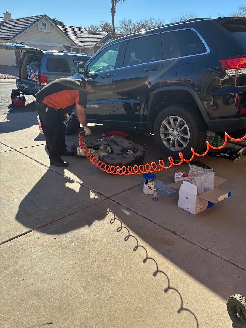 A mechanic works on a black SUV in a sunny driveway with tools scattered around.