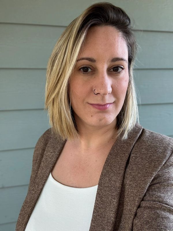 Woman with blonde bob haircut wearing a brown blazer and white top.