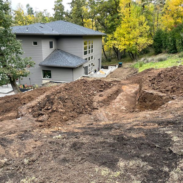 A modern house with a backyard under excavation surrounded by green trees.