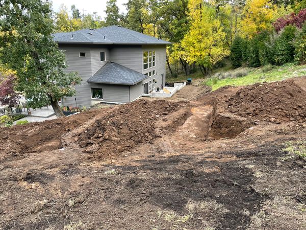 Backyard excavation near a modern house with trees in the background.