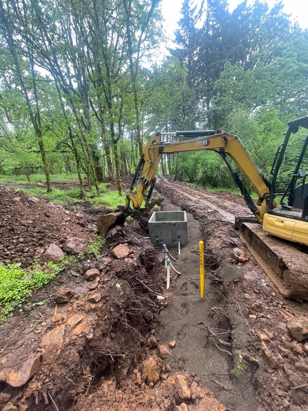 Excavator working on a trench in a forested area with construction equipment.