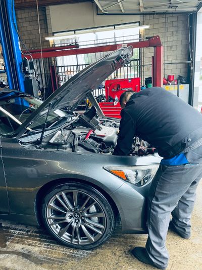Mechanic inspecting engine of a silver car in a garage.