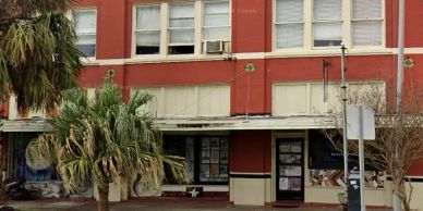Old red building with palm trees and posters in windows.