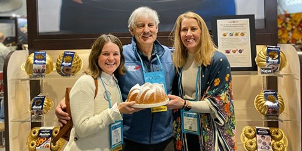 Heather, Mike, and Vanessa holiding a bundt cake by a Nordiware display. 