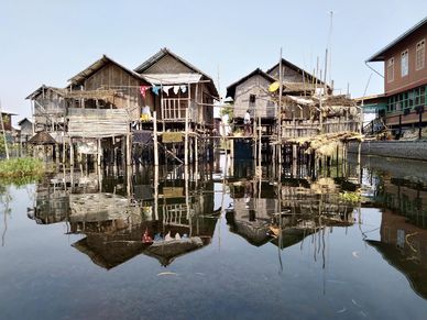 Two houses on wooden polls floating on still water with the houses reflection showing.