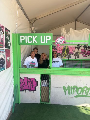Four people standing at a green pick-up booth with graffiti art.