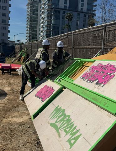 Workers in helmets inspecting graffiti on angled boards at a construction site.