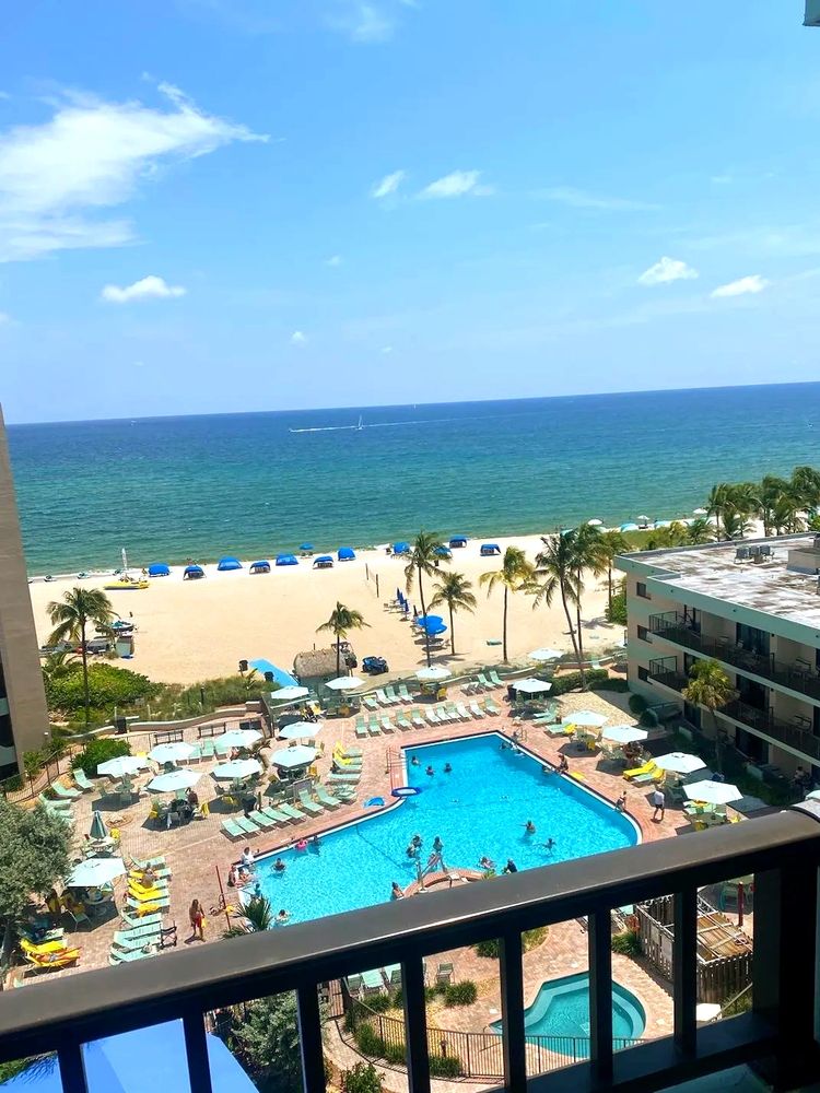 An aerial, sunny balcony view of Lighthouse Cove Resort's beachfront and pool amenities.
