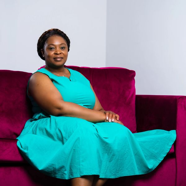 A woman in a turquoise dress sitting on a magenta couch.