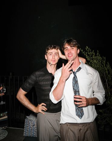 Two men posing, one smoking, the other holding a drink.