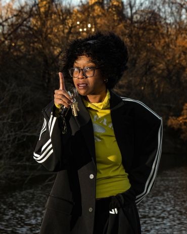 Woman in black coat pointing finger outdoors.