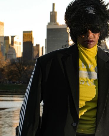 Person in sunglasses and hat with city background.