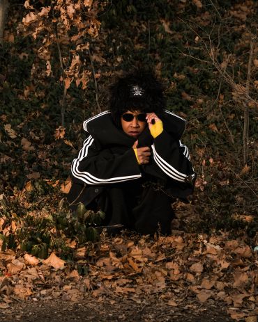 Person in dark clothing crouching in autumn leaves.