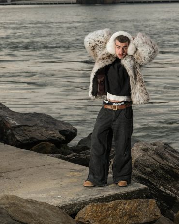 Man in fur coat and earmuffs near water.