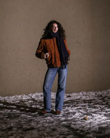 Woman standing on snowy ground at night with scarf and jacket.