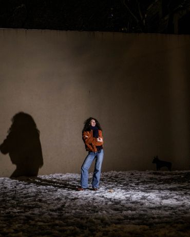 Person standing outdoors at night with large shadow.