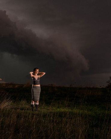 Woman standing in a field under dark, stormy skies.