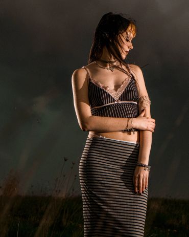 Woman in striped outfit posing outdoors under dark sky.