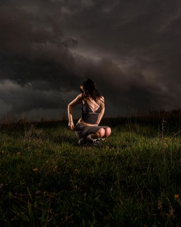 Woman sitting on grass under stormy sky.