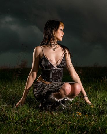 Woman crouching in grass under dark sky.