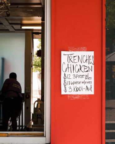 Sign advertising chicken meals and Kool-Aid on a red wall.
