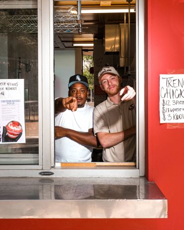 Two men pointing at the camera from a service window.