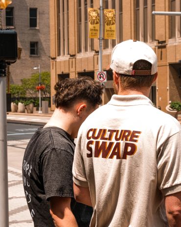 Two men standing on a city street, one with "CULTURE SWAP" shirt.