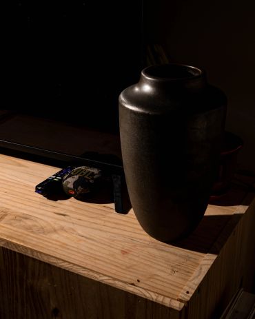 A dark vase on a wooden table with a remote and disc.