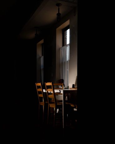 Sunlit wooden chairs and table by a window with curtains.