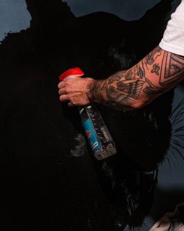 Tattooed arm spraying black paint on wall.