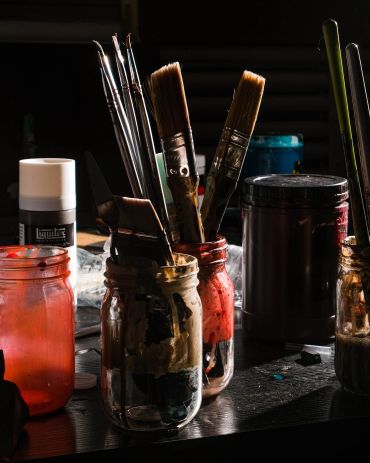 Paintbrushes and jars with paint on a table.