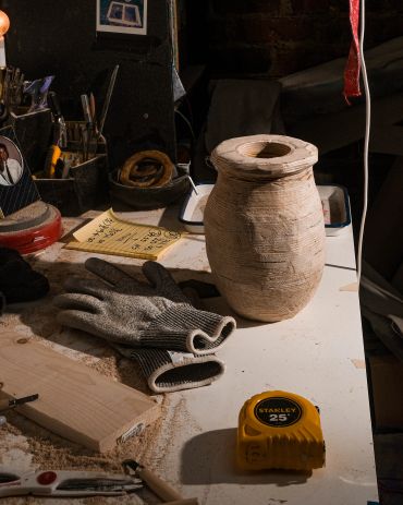 A wooden jar on a workbench with gloves and measuring tape.