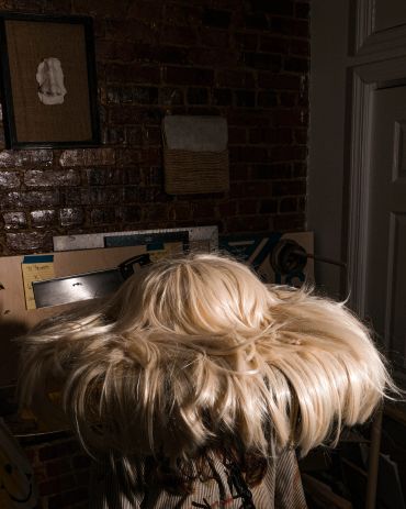 Back view of person with long, voluminous blonde hair in rustic room.
