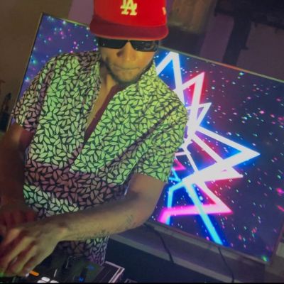 DJ wearing a patterned shirt and red LA cap mixing music.