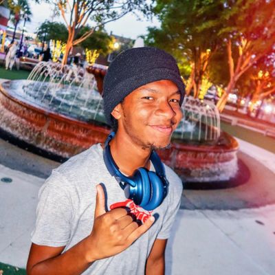 Young man smiling with headphones around his neck near a fountain.