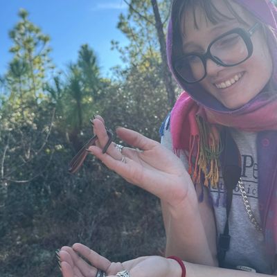 Smiling woman gently holding a praying mantis outdoors in nature.