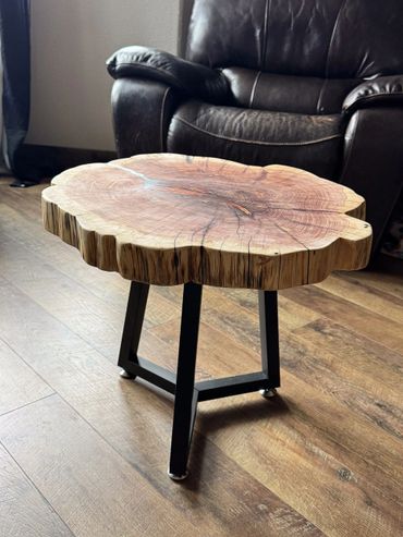 Rustic wooden side table with natural tree ring top and black metal legs.