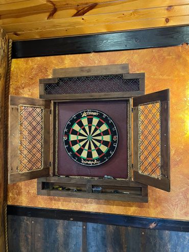 Dartboard mounted inside a wooden cabinet with open doors on a textured wall.
